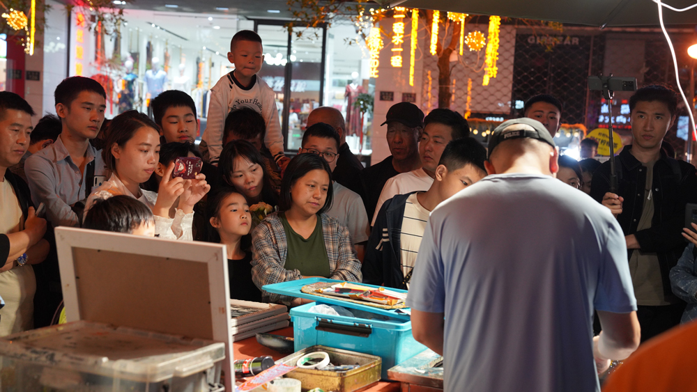 杭州拱墅區武林夜市上，攤主現場作畫，引得游客市民駐足觀賞。程欣攝